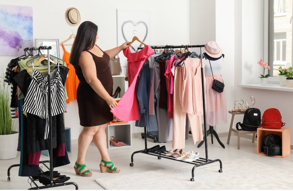 茶色のワンピースを着た女性が、ピンクのドレスを選んでいる様子。周囲には複数の洋服ラック